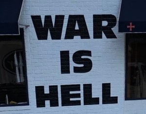 Photo of writing on the side of a wall that reads ‘War is Hell’  